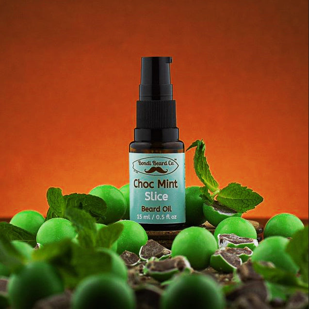 Image of Bondi Beard Co. spray bottle with Choc mint Slice Beard label. Spray bottle is surrounded by mint leaves and chocolate mint confectionery with bright orange background.